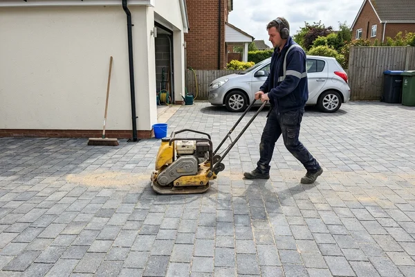 Installer running a plate compactor over finished block paving to bed the blocks