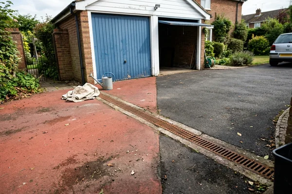 Red coloured tarmac driveway apron in front of a garage with a drainage channel